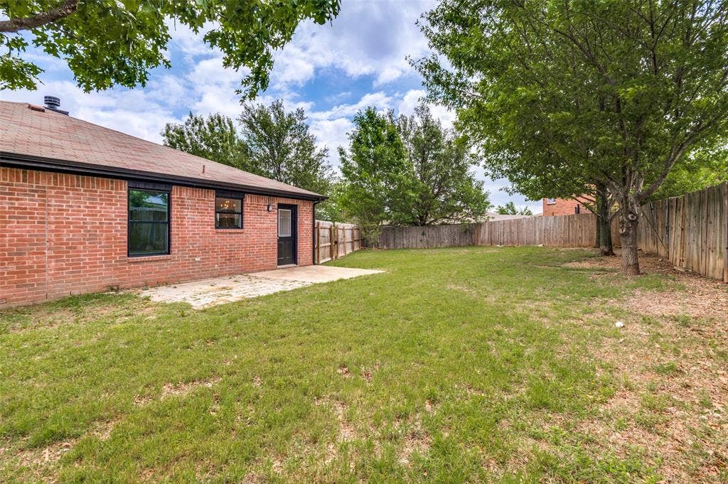 Expansive backyard featuring a red brick exterior, a concrete patio, a wood privacy fence, and mature trees