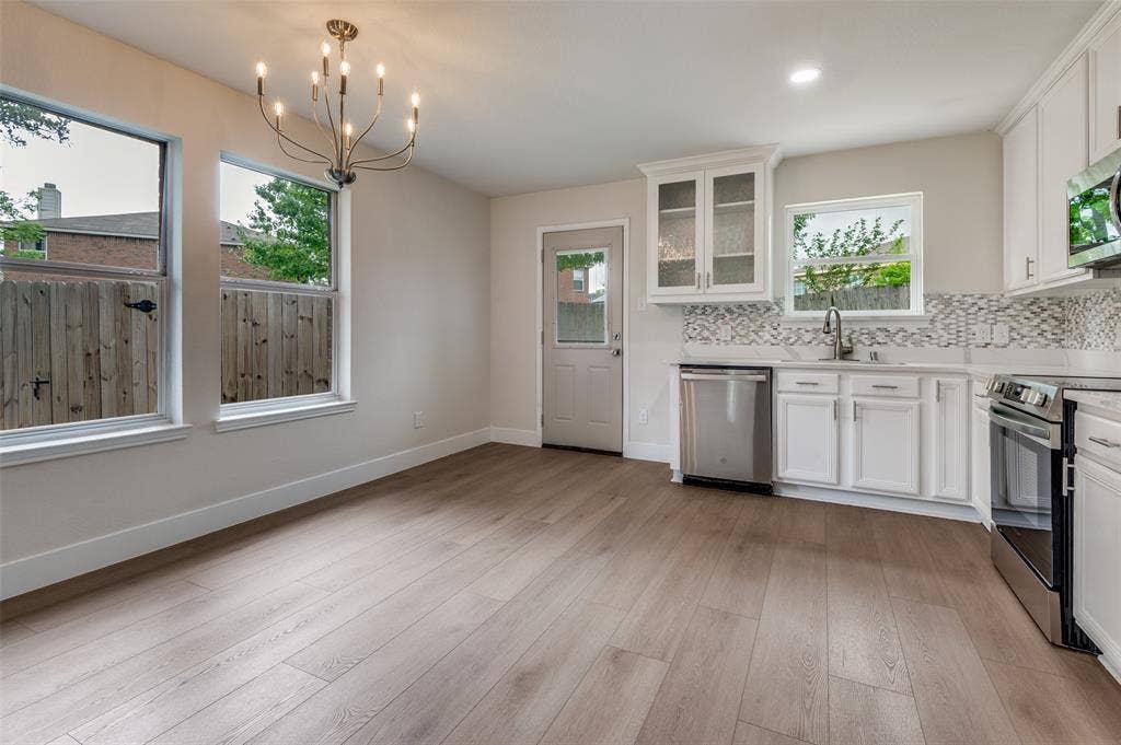 Open-concept kitchen and dining area featuring light wood-finish flooring, white cabinetry, stainless steel appliances, and a decorative tile backsplash