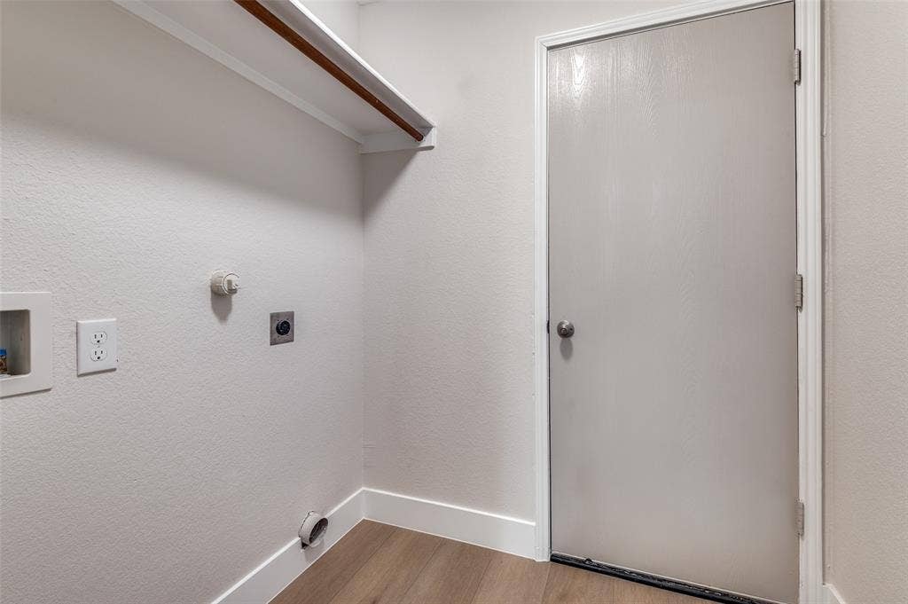 Dedicated utility area featuring wood-finish flooring, a built-in overhead shelf, white baseboards, and a light-toned door