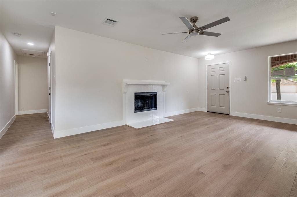 Open concept living space featuring wood-finish flooring throughout, a fireplace with white mantel and hearth, and a contemporary ceiling fan