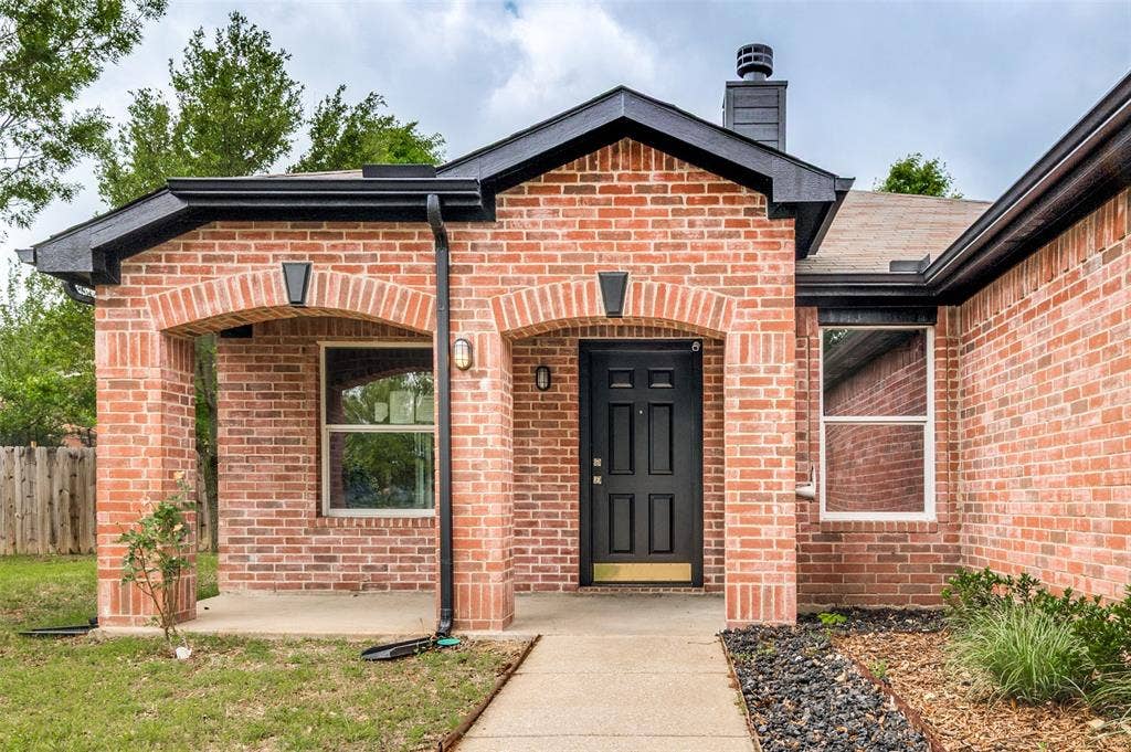 Brick exterior with a covered entry featuring arched brick columns, a black paneled front door, and a contrasting dark roofline with gutters