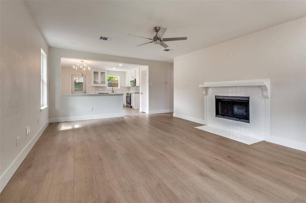 Open-concept living area featuring wood-finish flooring, a white brick fireplace with mantel, and a ceiling fan