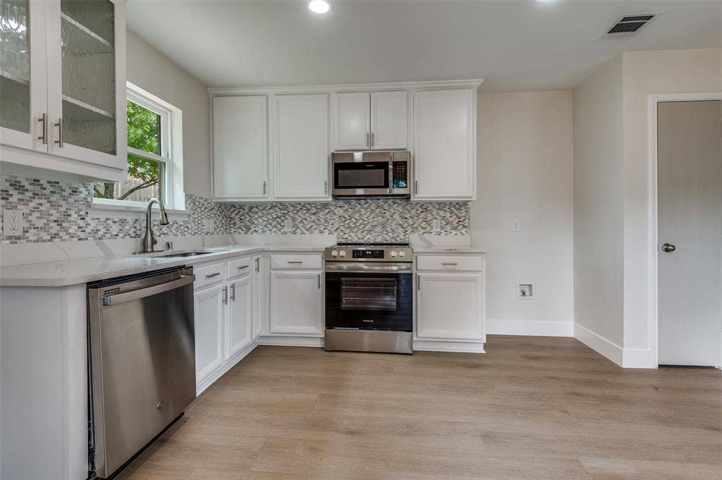 Kitchen featuring white shaker-style cabinetry with brushed nickel hardware, stainless steel appliances, and wood-finish flooring