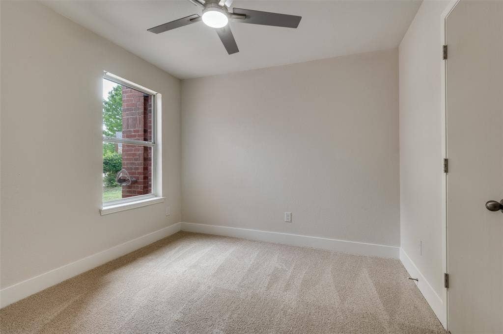 Carpeted room featuring a ceiling fan with integrated lighting, a single window with white trim, and a white interior door with bronze hardware