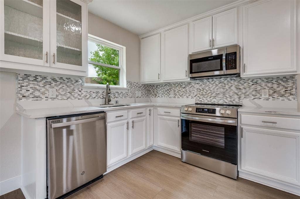 Updated kitchen featuring white shaker-style cabinetry, mosaic tile backsplash, stainless steel appliances, a stainless steel sink with a gooseneck faucet, and light wood-finish flooring