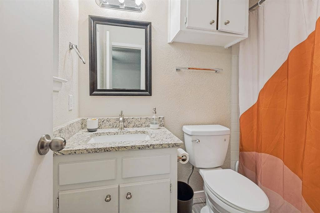 404 Green River Trail, Fort Worth, TX 76103 Bathroom featuring a white vanity with a granite-style countertop, undermount sink, and a framed mirror