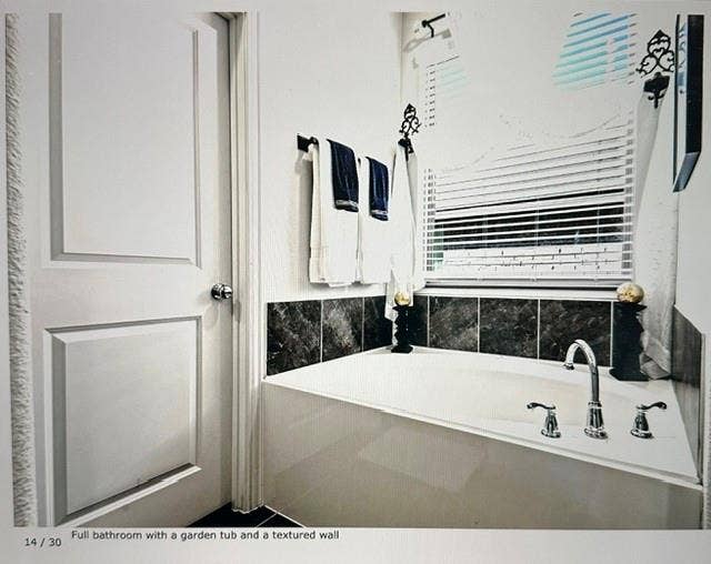 4220 Calla Drive, Forney, TX 75126 Garden tub with deck-mounted chrome fixtures, surrounded by dark tile accents and a window with horizontal blinds