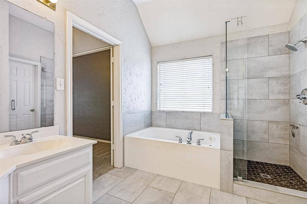 110 Falcon Creek Drive, McKinney, TX 75072 White soaking tub with chrome fixtures, a tiled shower with glass enclosure, and a single vanity with a white countertop and chrome faucet
