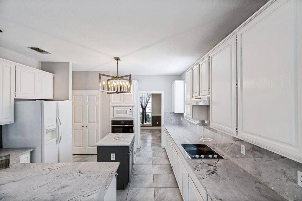 110 Falcon Creek Drive, McKinney, TX 75072 Kitchen featuring a central island with a dark base, light-toned countertops, white cabinetry, a built-in cooktop, and tile flooring