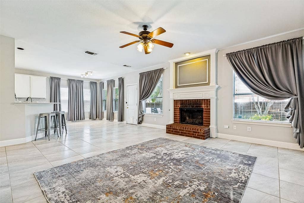 110 Falcon Creek Drive, McKinney, TX 75072 Spacious living area featuring a brick fireplace with a white mantel, ceiling fan, and light-toned tile flooring