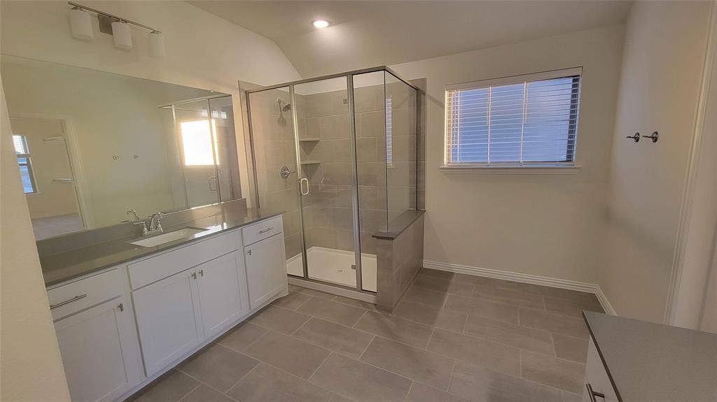 11346 Sugarlands Drive, Frisco, TX 75035 Bathroom featuring a glass-enclosed shower with a built-in bench, a spacious vanity with a single basin sink and stone countertop, white shaker-style cabinetry, and large format tile flooring