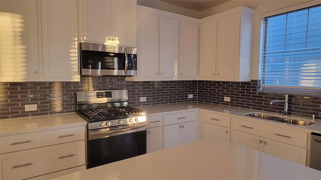 11346 Sugarlands Drive, Frisco, TX 75035 Modern kitchen featuring white shaker cabinetry, stainless steel appliances, a subway tile backsplash, and light-toned countertops