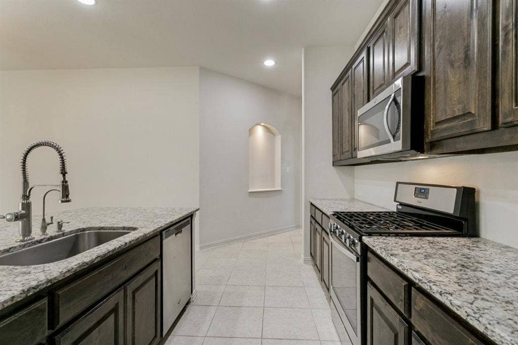 Kitchen featuring dark wood cabinetry, light speckled countertops, stainless steel appliances, and a built-in kitchen sink with a high-arc faucet