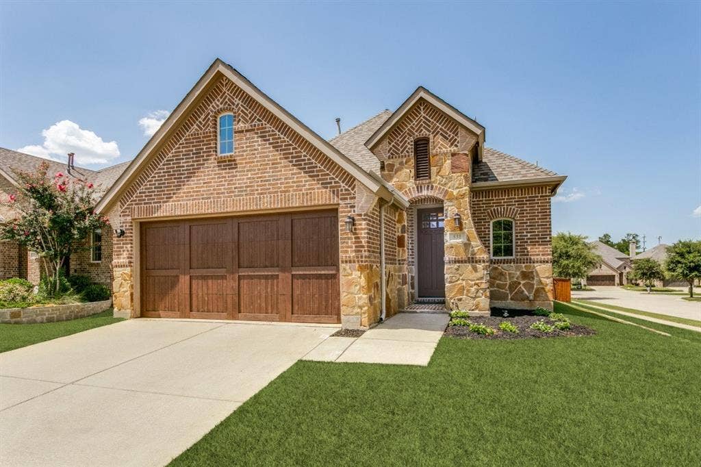 Brick and stone facade featuring an arched entry, a two-car wood-finish garage door, and a concrete driveway