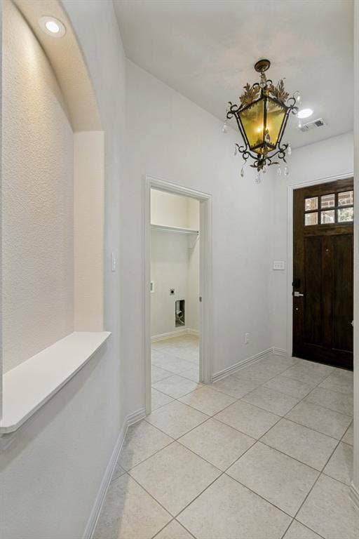 Foyer featuring light-toned square tile flooring, a decorative chandelier, and a dark wood entry door with glass inserts