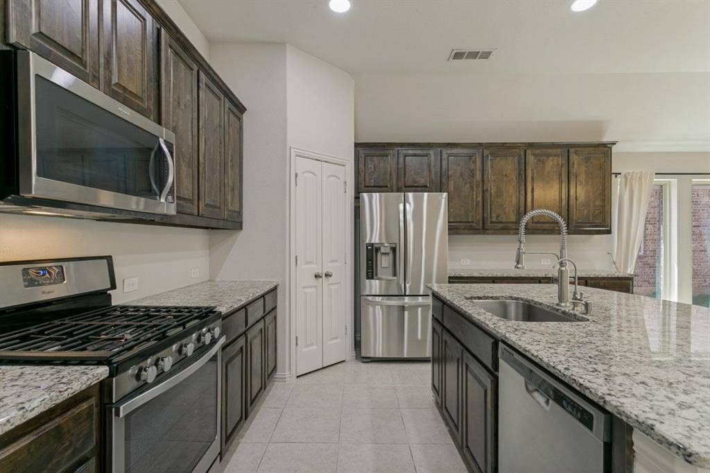 Modern kitchen featuring dark wood cabinetry, stainless steel appliances, granite countertops, and light tile flooring