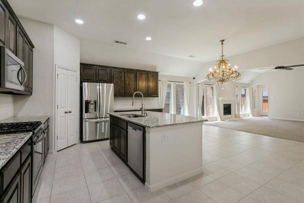 Open-concept kitchen featuring granite countertops, dark wood cabinetry, stainless steel appliances, and a central island with a sink