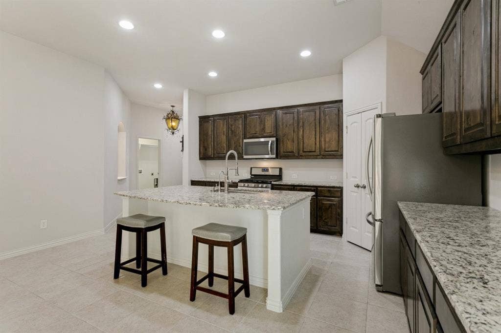 Kitchen featuring a central island with a granite countertop, dark wood-finish cabinetry, stainless steel appliances, and recessed lighting