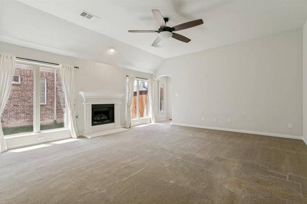 Spacious living area featuring a central fireplace with an ornate white mantel, vaulted ceiling, and a dark-bladed ceiling fan