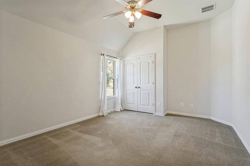 Carpeted room featuring a vaulted ceiling with a ceiling fan, a window, and double doors