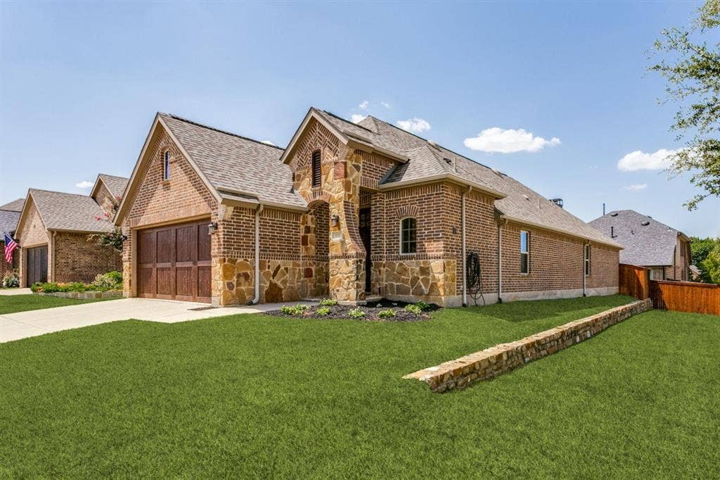 Brick and stone exterior featuring an arched entryway, gabled rooflines, and a two-car garage with wood-finish doors