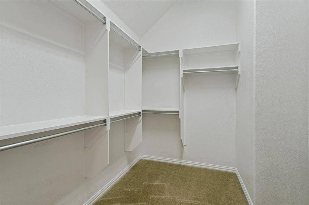 Walk-in closet with multiple white shelving units, chrome hanging rods, and a sloped ceiling