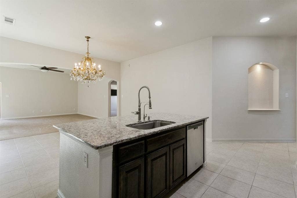 Kitchen island with granite countertop, undermount stainless steel sink, and dark wood cabinetry