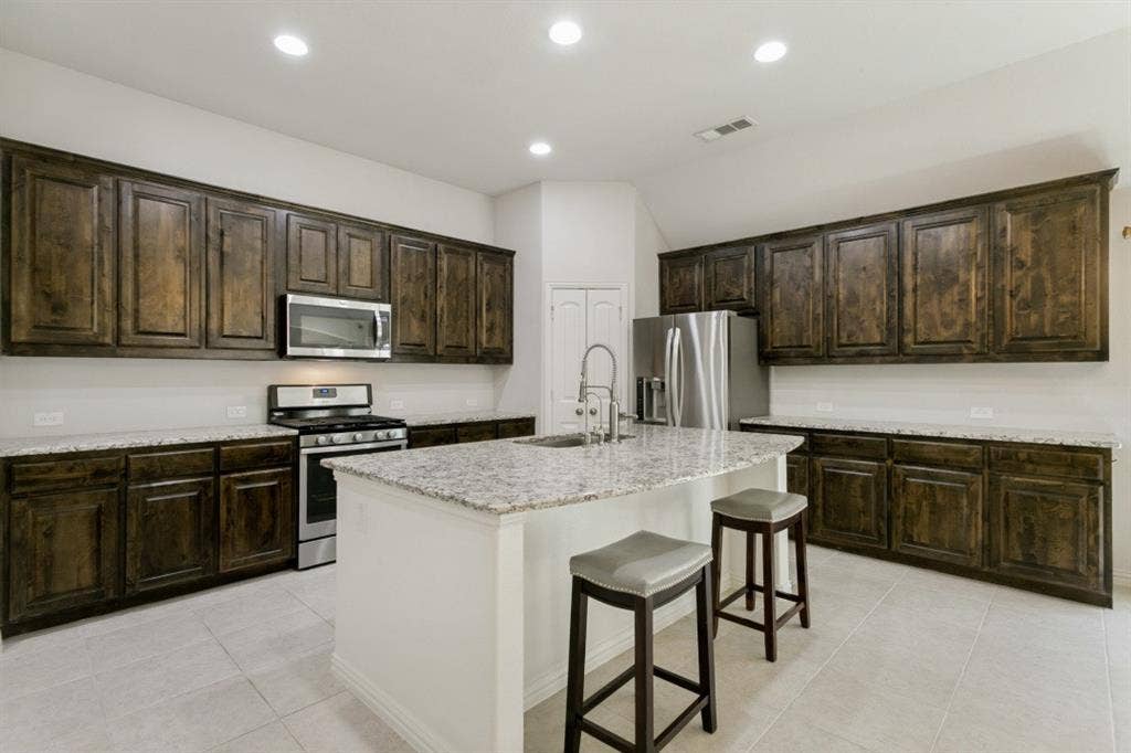 Kitchen featuring dark wood cabinetry, tons of granite countertops, and a central island with a sink and deluxe faucet.  Also included for you is a stainless steel refrigerator