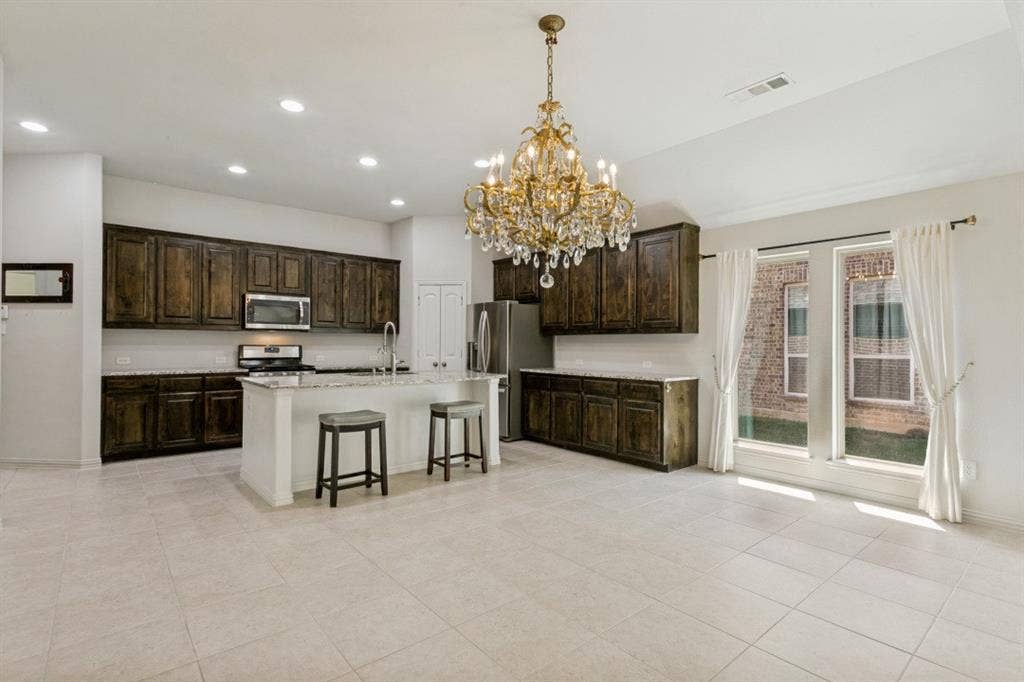 Open-concept kitchen featuring an island with seating, dark wood cabinetry, light countertops, stainless steel appliances, and a decorative chandelier