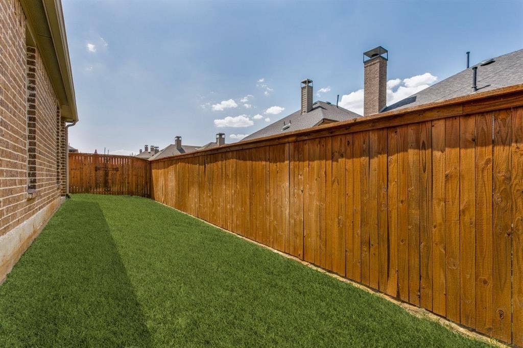 Fenced backyard featuring a manicured lawn, brick exterior siding, and a wooden privacy fence