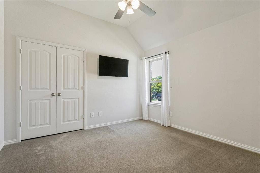 Carpeted room featuring a vaulted ceiling and a ceiling fan with light fixture