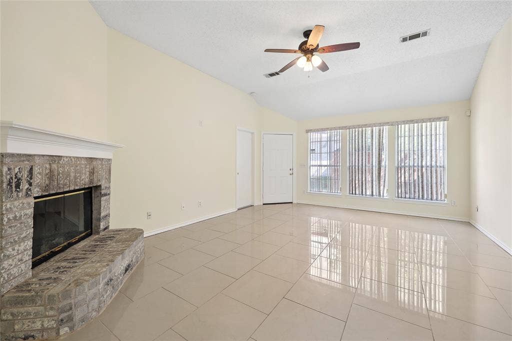 113 Bridlegate Drive, McKinney, TX 75069 Vaulted ceilings with a ceiling fan, stone-surround fireplace, large-format tile flooring, and oversized windows with vertical blinds
