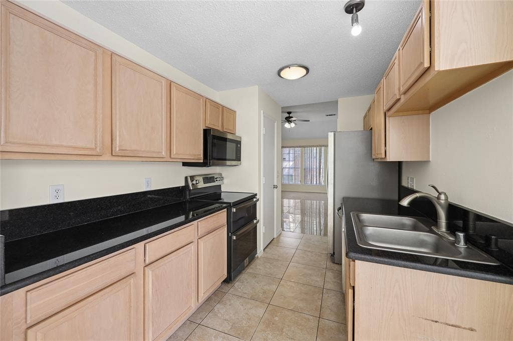 113 Bridlegate Drive, McKinney, TX 75069 Kitchen featuring light-finish cabinetry, dark stone countertops, stainless steel appliances, dual-basin sink with high-arch faucet, and tile flooring