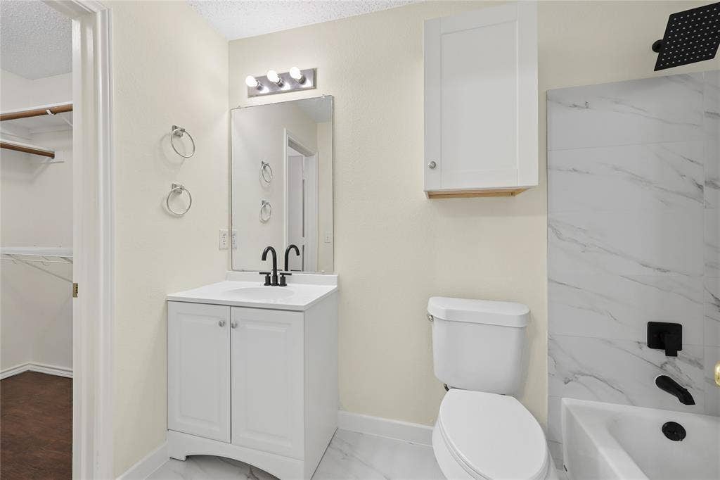 113 Bridlegate Drive, McKinney, TX 75069 Bathroom featuring a white vanity with a rectangular sink, matte black fixtures, a wall-mounted storage cabinet, and tub surround with stone-finish tile