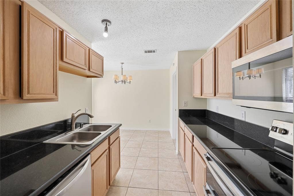 113 Bridlegate Drive, McKinney, TX 75069 Kitchen featuring flat-panel wood cabinetry, black solid-surface countertops, dual-basin stainless steel sink, ceramic tile flooring, and built-in microwave