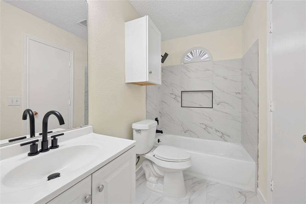 113 Bridlegate Drive, McKinney, TX 75069 Bathroom featuring a white vanity, matte black widespread faucet, stone-patterned tile tub surround with an integrated niche, and an arched transom window