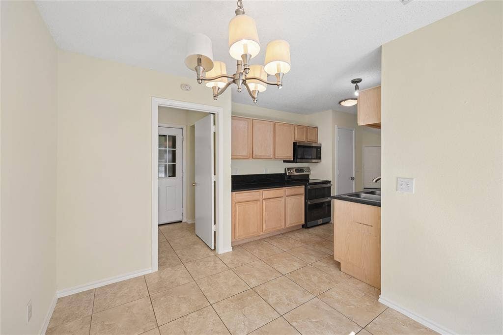 113 Bridlegate Drive, McKinney, TX 75069 Kitchen featuring light-finish cabinetry, dark solid-surface countertops, built-in black appliances, tile flooring, and a multi-arm chandelier