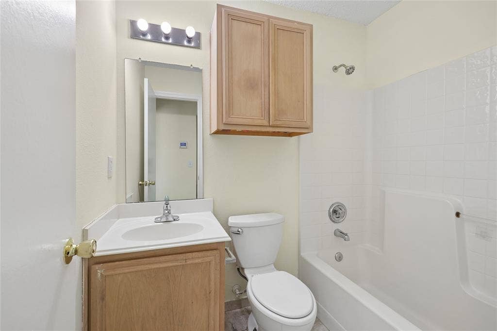 113 Bridlegate Drive, McKinney, TX 75069 Bathroom featuring a vanity with a white countertop and integrated sink, wall-mounted upper cabinetry, a chrome three-light fixture, a rectangular mirror, and a tub-shower combination with white wall surround