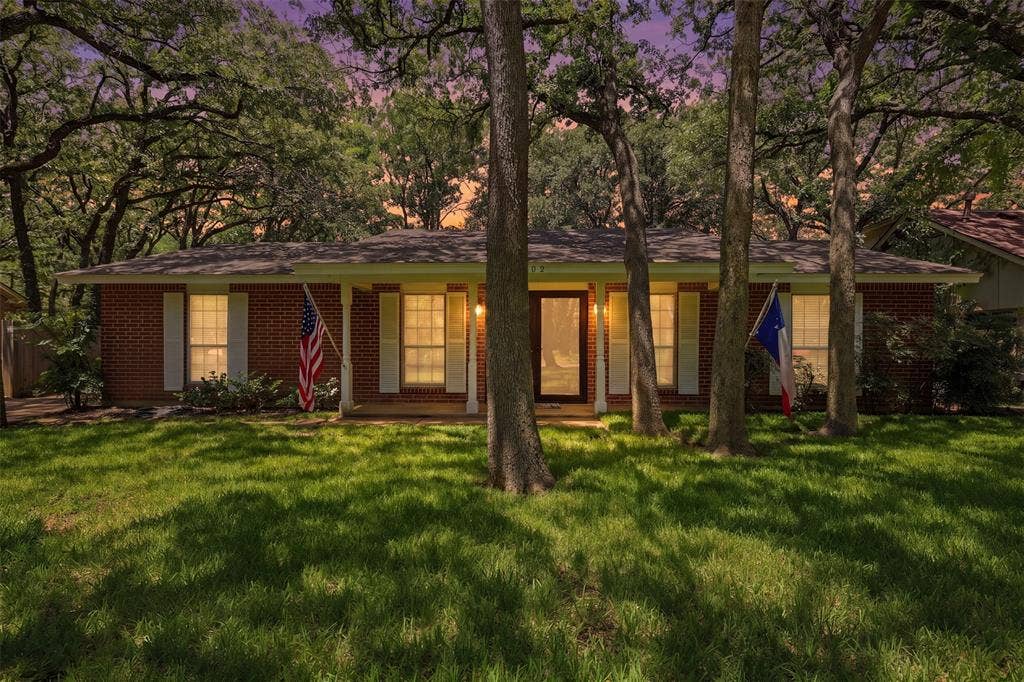 3702 Hastings Drive, Arlington, TX 76013 Twilight view of this inviting single-story Woodland West home, showcasing warm exterior lighting, mature trees, and classic brick architecture
