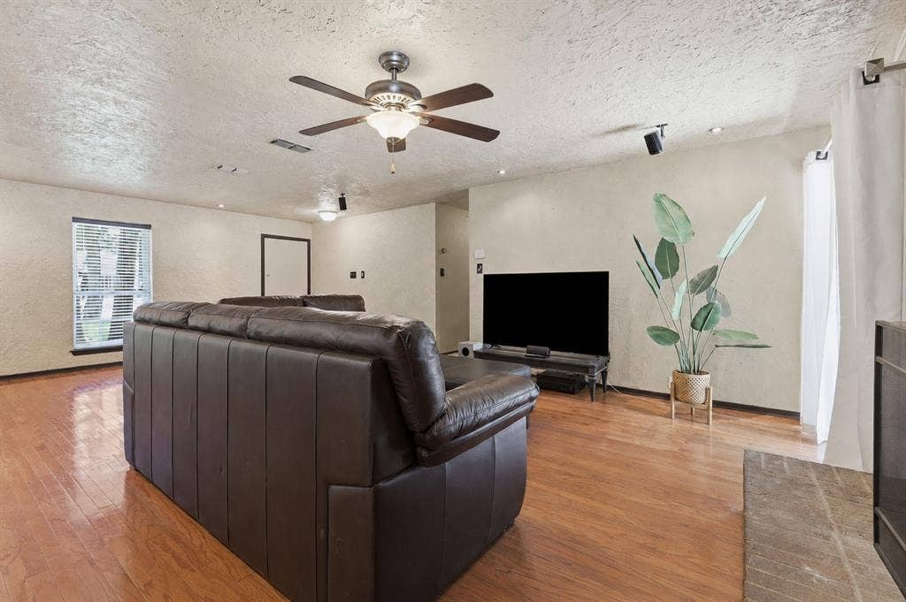 3702 Hastings Drive, Arlington, TX 76013 Spacious living room centered around a brick fireplace, with wood flooring, abundant lighting, and access to the backyard patio