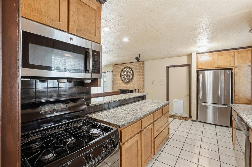 3702 Hastings Drive, Arlington, TX 76013 Kitchen with gas range, built-in microwave, granite counters, ample cabinetry, and a raised breakfast bar overlooking the living room fireplace