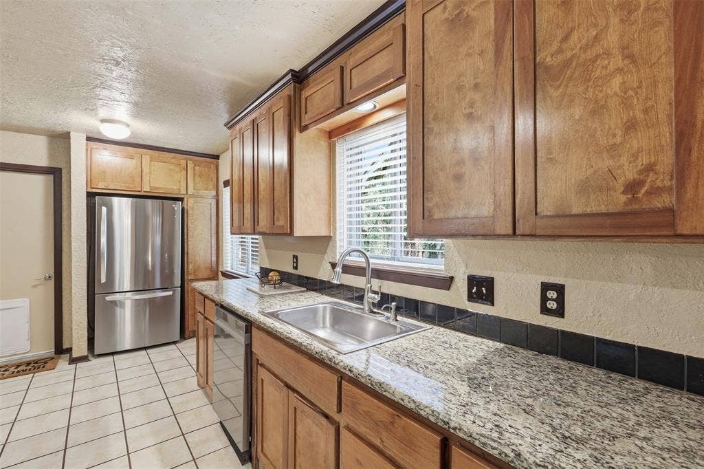 3702 Hastings Drive, Arlington, TX 76013 Galley-style kitchen with granite countertops, wood cabinetry, double sink, tile flooring, and multiple windows.