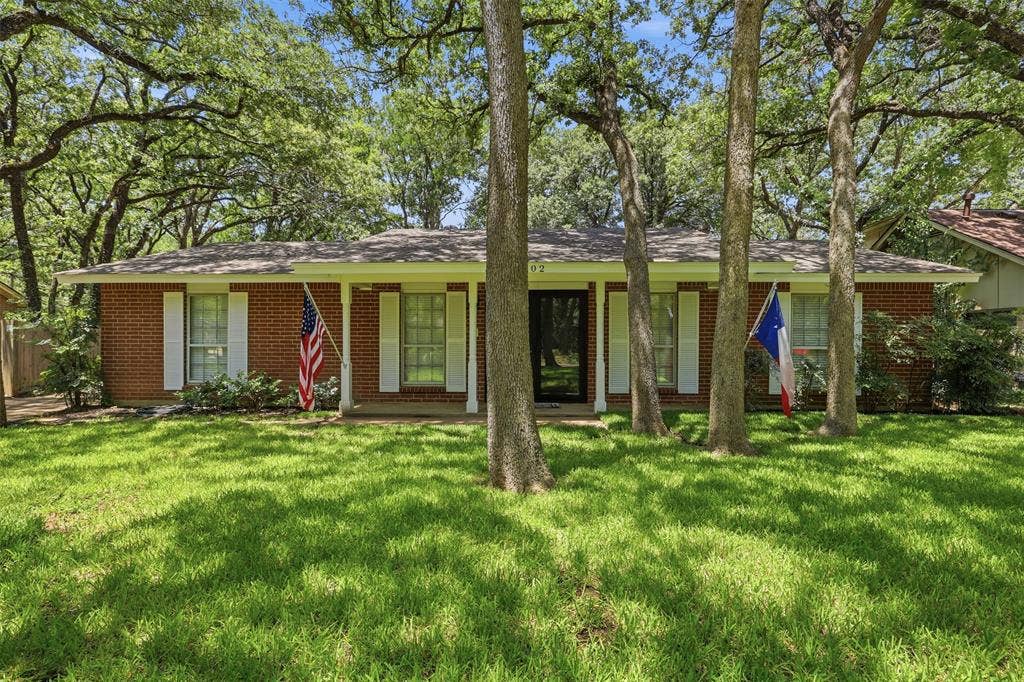 3702 Hastings Drive, Arlington, TX 76013 Established Woodland West home with classic brick exterior, covered front porch, mature trees, and a spacious front lawn