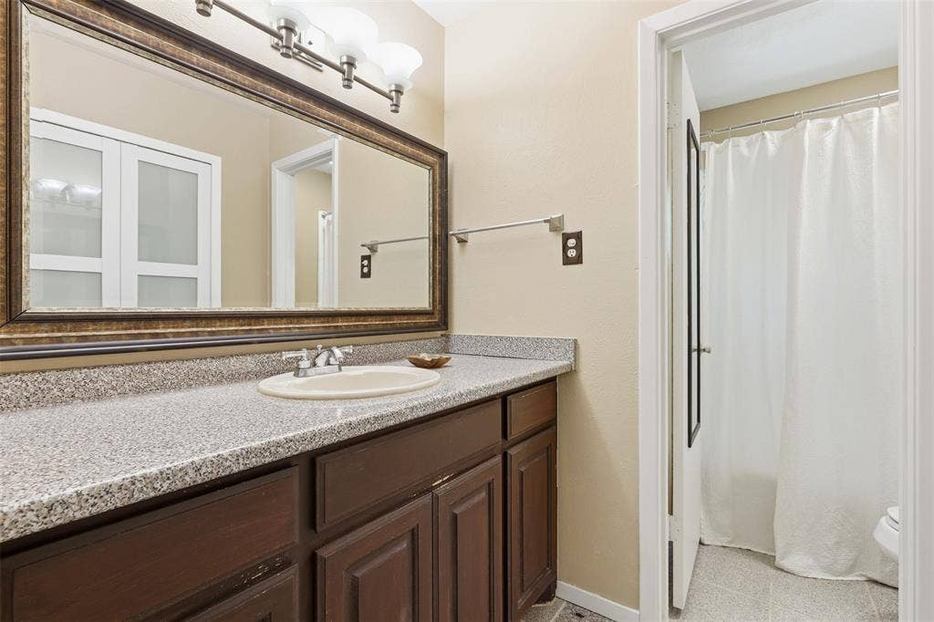 3702 Hastings Drive, Arlington, TX 76013 Functional bathroom vanity area featuring generous counter space, dark wood cabinetry, a large mirror, and built-in linen storage