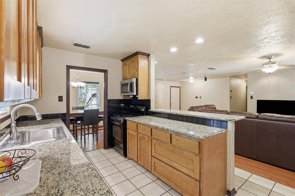 3702 Hastings Drive, Arlington, TX 76013 Galley-style kitchen with granite countertops, wood cabinetry, double sink, tile flooring, and multiple windows.