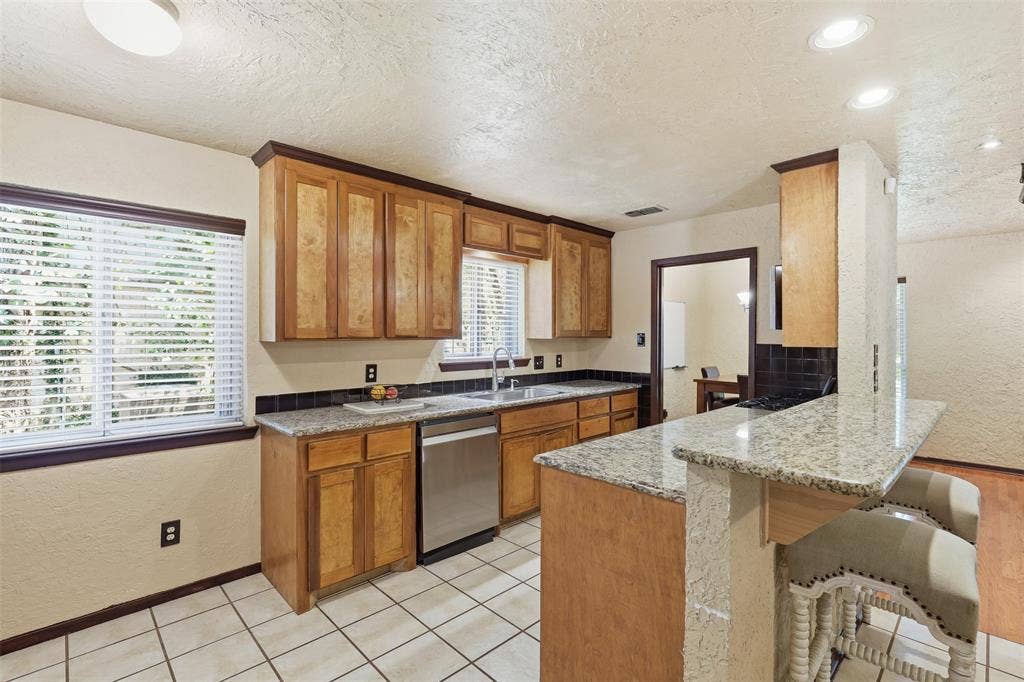 3702 Hastings Drive, Arlington, TX 76013 Galley-style kitchen with granite countertops, wood cabinetry, double sink, tile flooring, and multiple windows.
