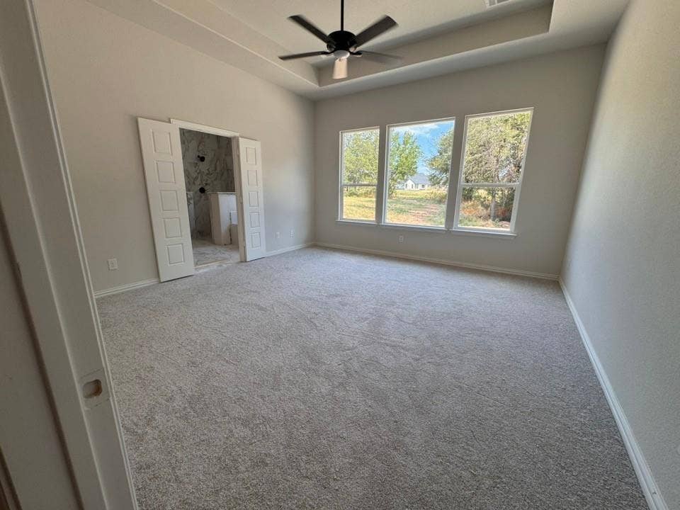 809 Zachary Michael Court, Springtown, TX 76082 Spacious room featuring light-toned carpeting, a tray ceiling with a ceiling fan, and three large windows