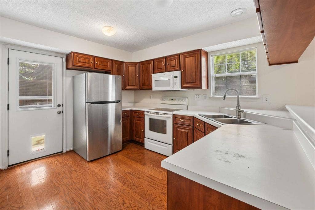 Kitchen featuring wood-finish flooring, rich wood cabinetry, stainless steel refrigerator, white electric range with overhead microwave, and a double basin sink