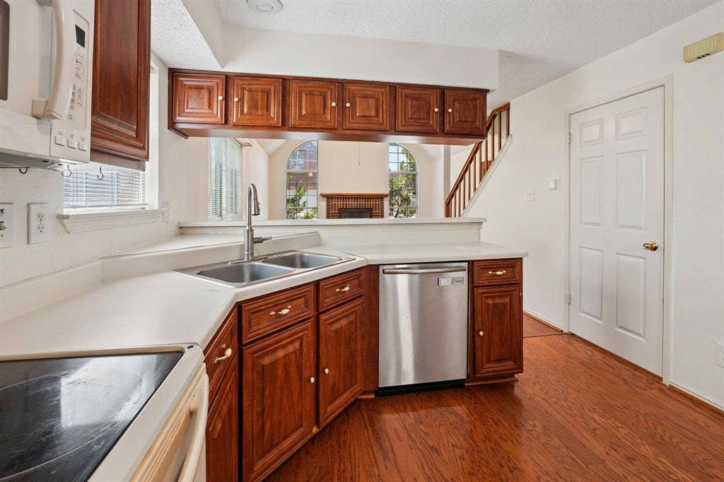 Kitchen featuring wood-finish flooring, wood cabinetry with gold-tone hardware, white countertops, and a stainless steel dishwasher