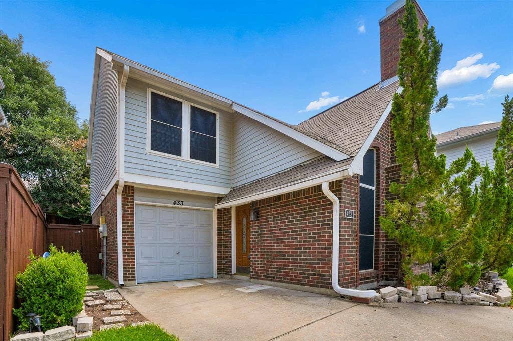Brick and siding exterior featuring an attached garage with a drive, a tall brick chimney, and a side fence